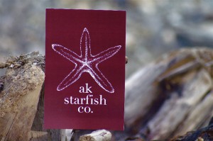 AK Starfish Logo of Starfish in white on red background sitting on a piece of driftwood, Princess Lodges