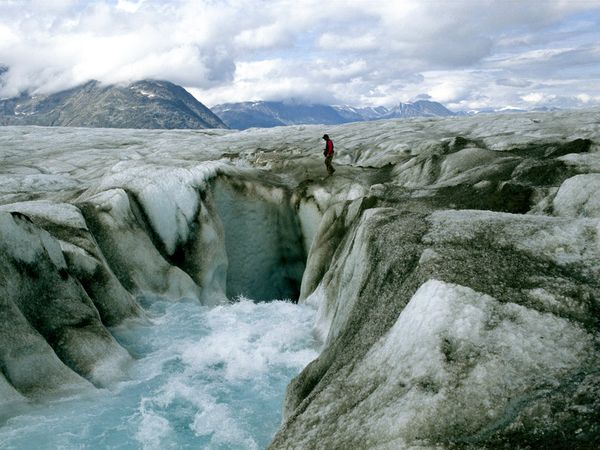 a man hiking across a glacier with rapids running below. 