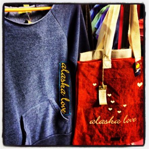 A blue long sleeve shirt and red bag on display with alaska love written on both, Princess Lodges