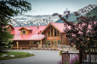 Exterior photo of Kenai Princess Wilderness Lodge shown from the main entrance with mountains behind