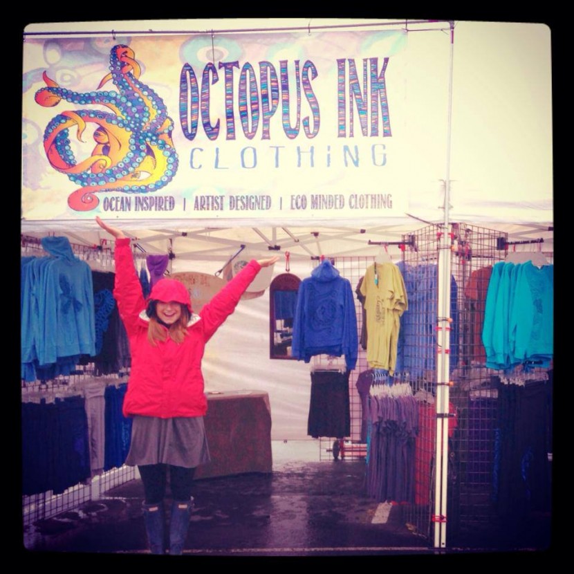 Woman with arms raised in front of booth for Octopus Ink clothing in Anchorage Alaska